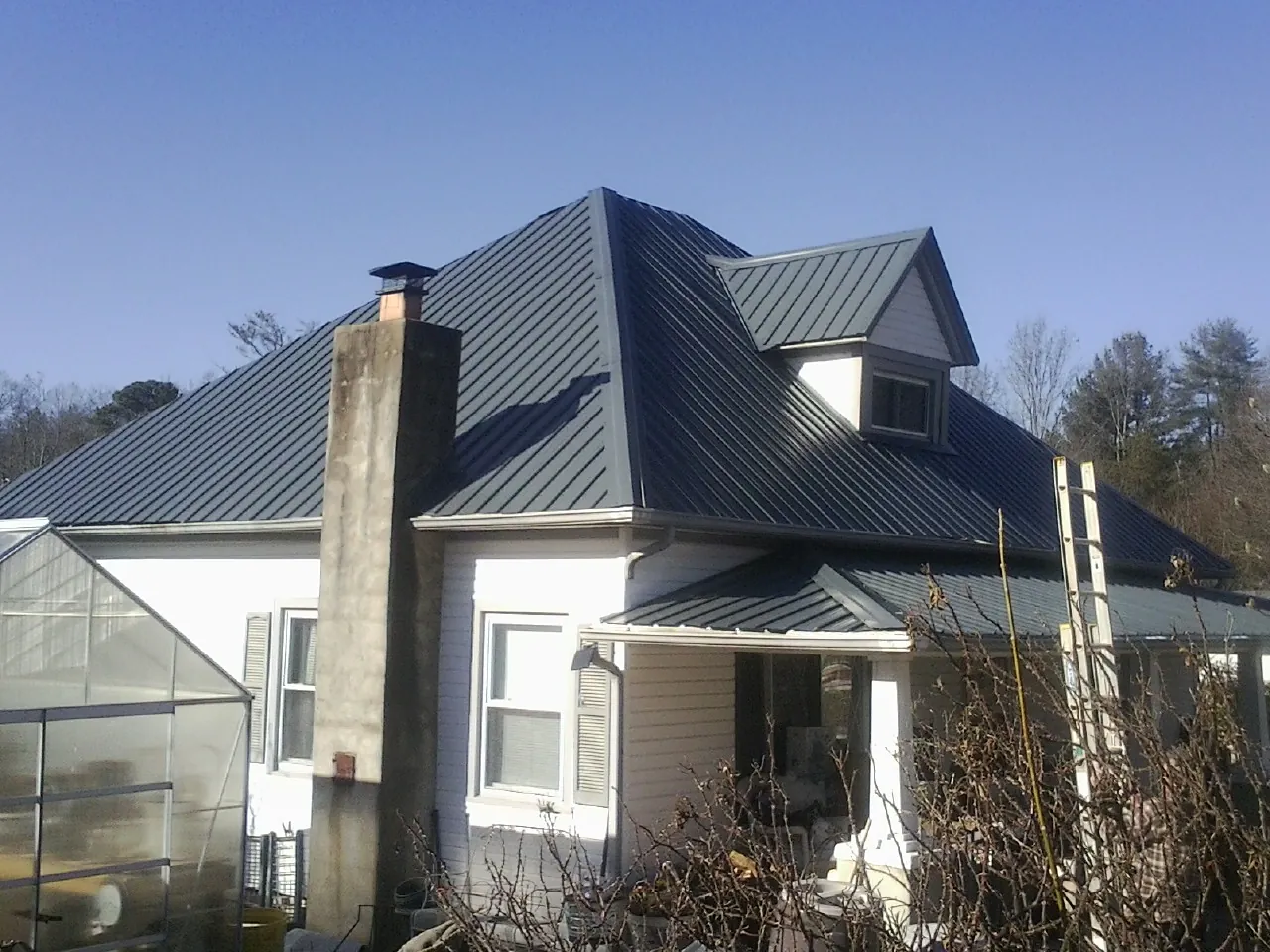 Dark blue standing seam metal roof on a white farmhouse with dormer — Slate & Tile Roof Repair by Roofing Brothers in Radford