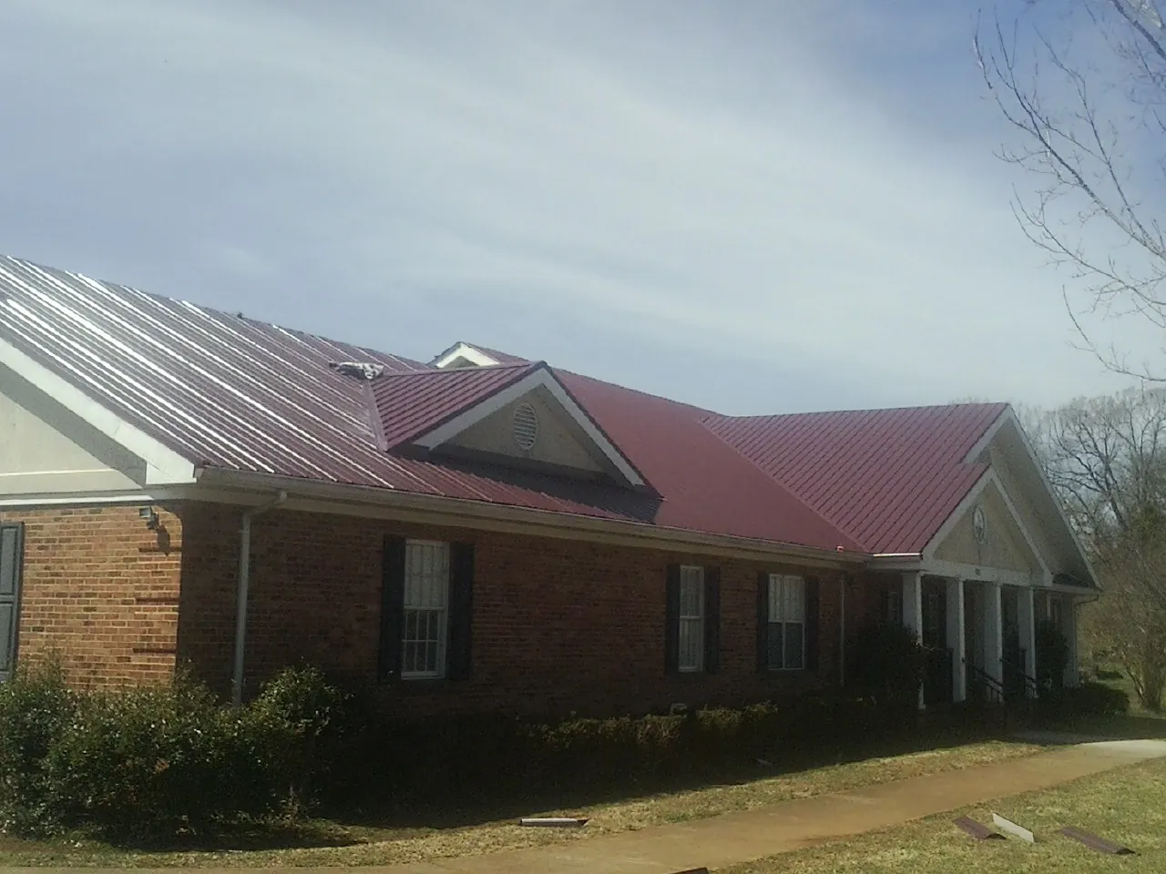 Red metal roof with gabled entries on a long brick building, from a Hail Damage Roof Repair job in Radford