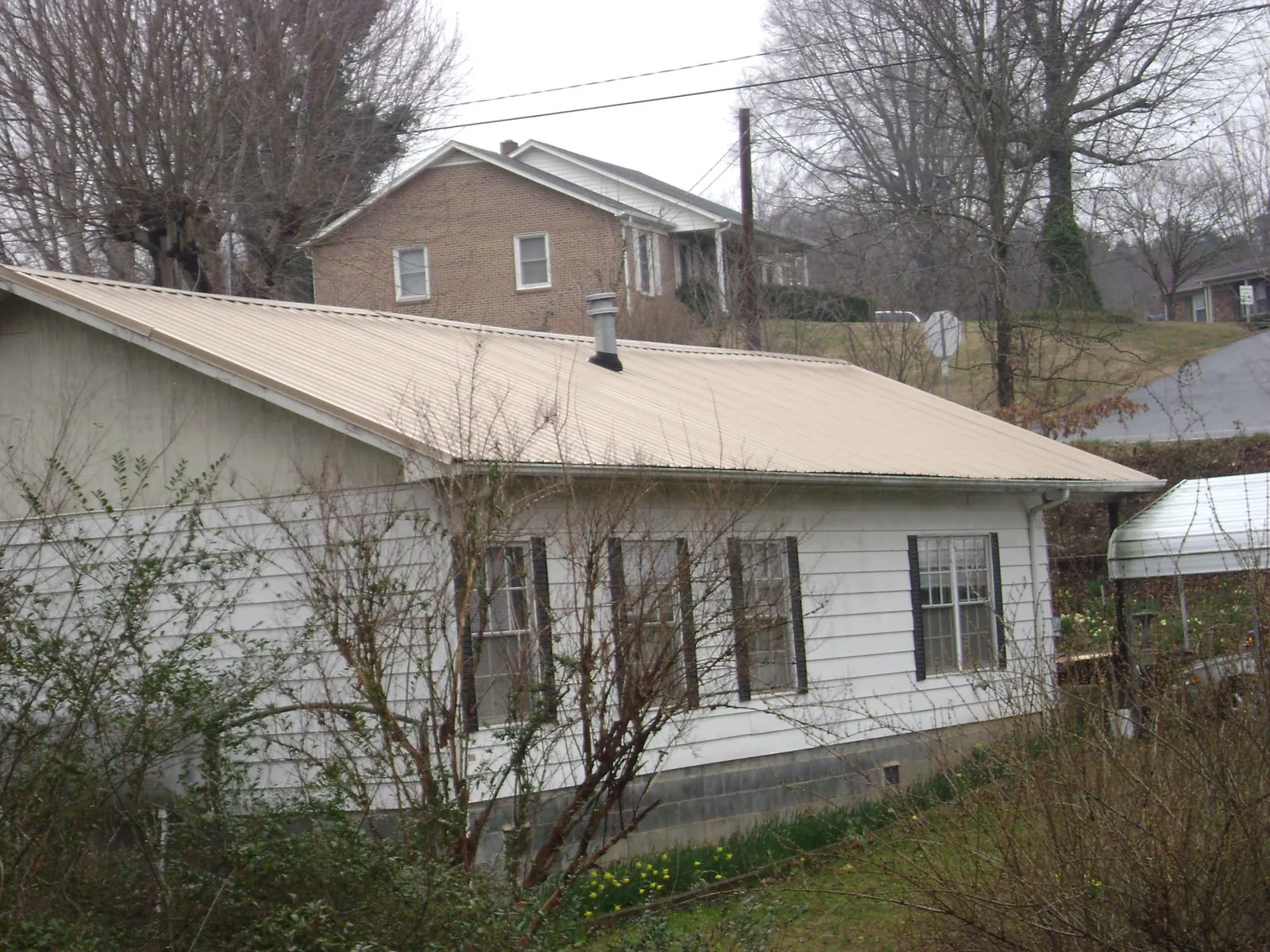 Tan metal roof on a white sided house set into a hillside — Commercial Roofing by Roofing Brothers in Radford