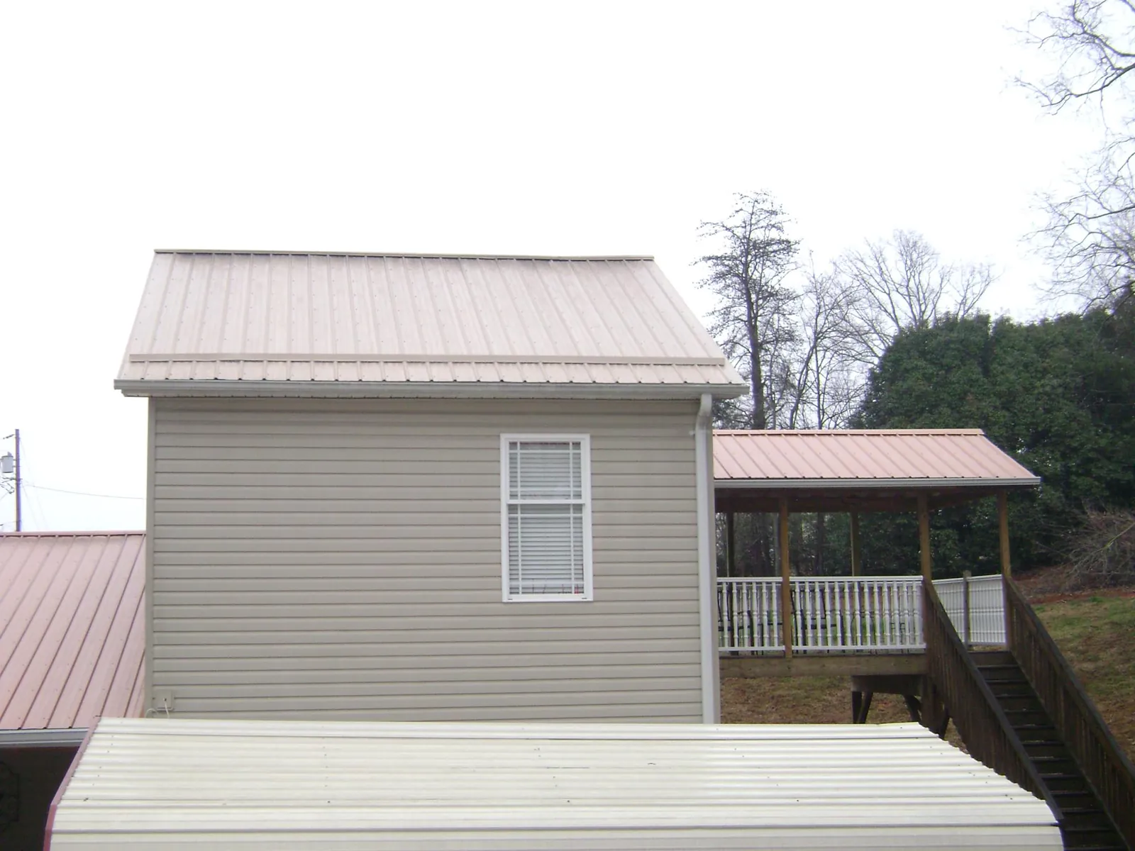 Tan metal roofs on a two story addition and attached porch, from a Roof Replacement job in Radford